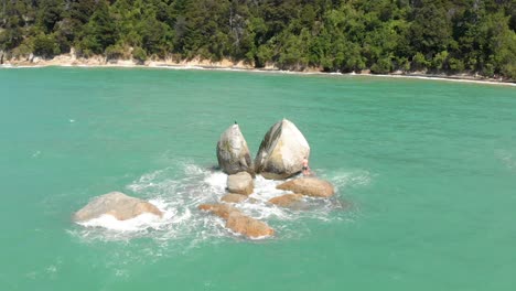 Aerial-clip-of-a-portion-of-the-ocean-in-the-Abel-Tasman-National-Park,-with-a-rock-in-the-foreground-with-the-curious-form-of-a-split-apple