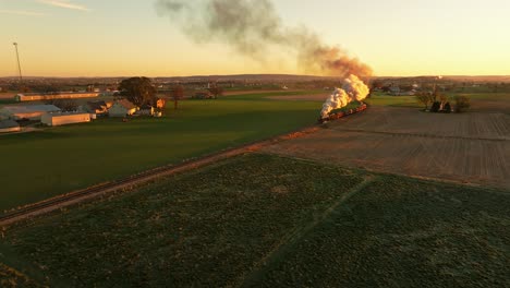 Drone-View-of-a-Steam-Engine-Approaching-Blowing-Lots-of-Smoke-at-Sunrise-Traveling-Thru-the-Farmlands-on-Fall-Morning