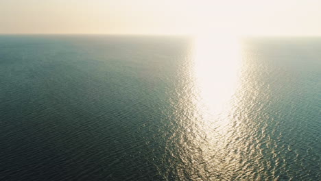 High-Aerial-Drone-Shot-into-the-Sun-of-Stunning-Beautiful-Sunset-Over-Calm-Still-Sea-with-Small-Waves