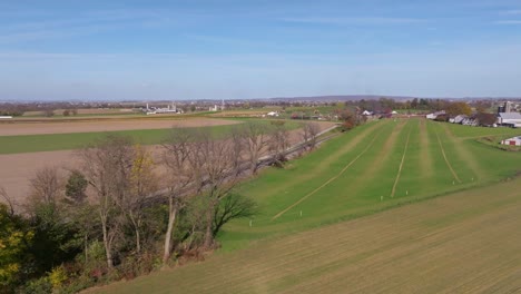 An-Aerial-View-of-a-Single-Rail-Road-Track-Going-Thru-Country-Farmlands-as-a-Steam-Train-Approaches-in-the-Distance-on-a-Sunny-Fall-Day
