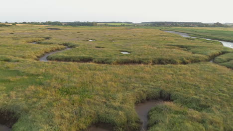 Low-Aerial-Drone-Shot-Flying-Over-Fairly-Dry-Green-Salt-Marsh-at-Sunset-in-North-Norfolk-UK
