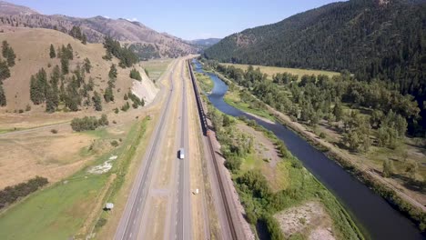 Arial-shot-of-train-driving-along-river-and-highway