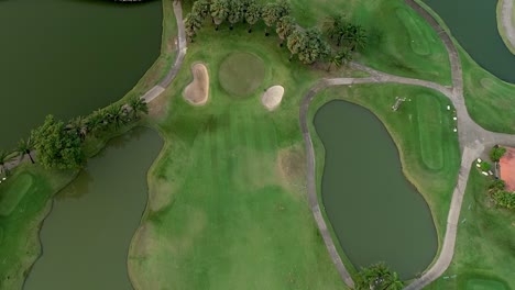 Golf-Course-Pond-Surrounded-By-Lush-Grassland-and-Narrow-Path-On-Thailand,-Bangkok--aerial-shot