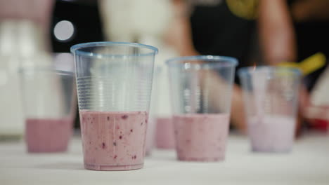 Close-up-of-a-couple-of-cups-with-tasty-healthy-and-fruity-red-pink-strawberry,-blueberry,-avocado-and-raspberry-smoothie-on-a-white-table-top
