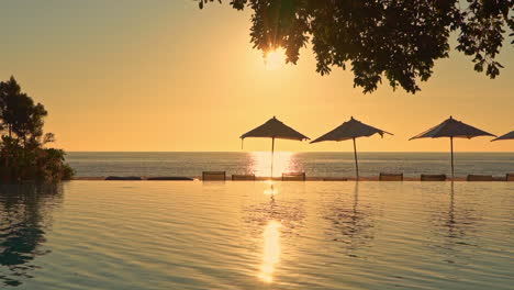 Meerblick-Von-Einem-Tropischen-Resort-Mit-Swimmingpool-Und-Sonnenschirmen-Im-Vordergrund-Und-Goldenem-Sonnenuntergang-Und-Ozean-Im-Hintergrund