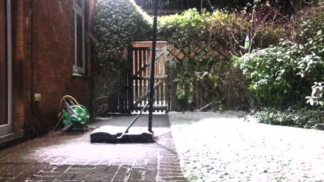 Snow-falling-in-backgarden-with-wooden-gate-near-the-base-of-a-netball-hoop-and-a-coiled-hose