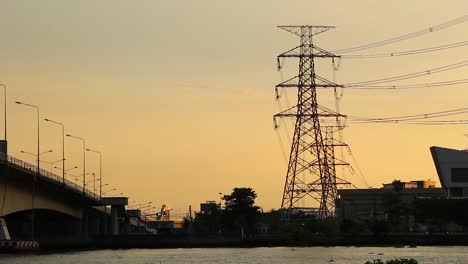 High-voltage-power-line-at-the-side-of-river-during-sunset