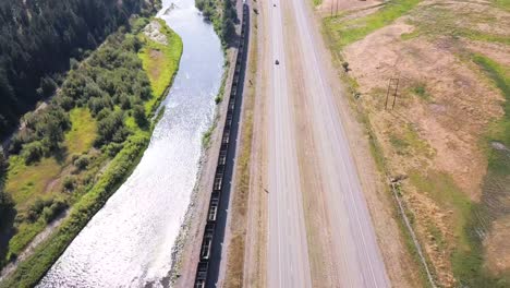 Arial-shot-of-train-driving-along-highway-and-river-on-USA's-westcoast