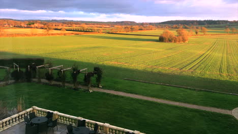 Leicestershire-Manor-House-diagonally-overlooking-golden-field-with-courtyard-with-alfresco-setting-and-stone-fence