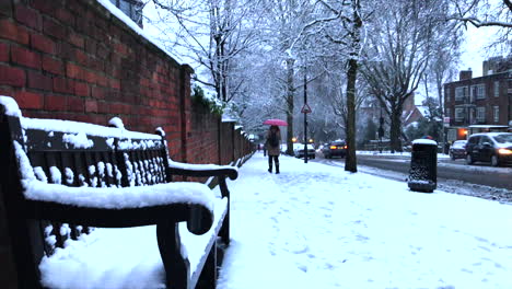 Snowy-London-city-scene-with-snow-piled-up-on-a-bench-and-person-with-a-Red-Umbrella