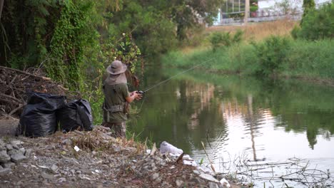 A-local-man-fishing-in-a-small-canal-in-Pathum-Thani,-Thailand---wide-shot
