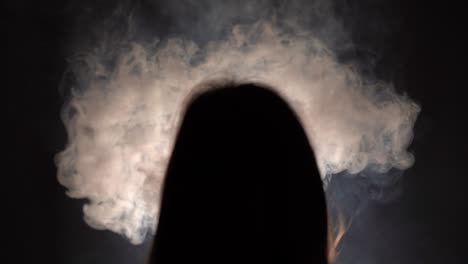 Isolated-slow-motion-silhouetted-closeup-of-a-person-with-long-hair-binge-smoking-in-a-dark-room-facing-a-dark-wall