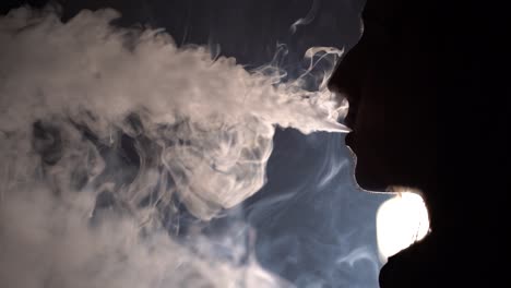 Slow-motion-isolated-silhouetted-closeup-profile-view-of-a-man-smoking-and-blowing-out-a-lot-of-smoke-in-dark-background