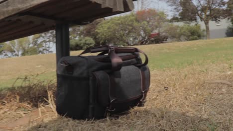 A-small-camera-bag-left-on-the-grass-under-a-wooden-bench