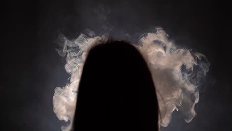 Isolated-silhouetted-closeup-of-a-person-with-long-hair-binge-smoking-in-a-dark-room-facing-a-dark-wall