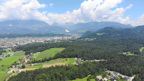 Aerial:-High-altitude-flight-over-Arboretum-in-Volcji-Potok,-with-vast-forest-and-mountain-range-in-the-background