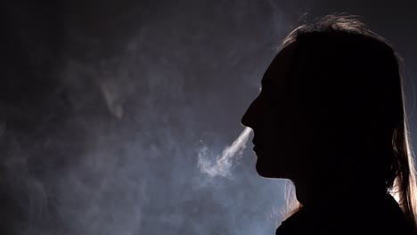 Isolated-silhouetted-closeup-side-view-of-a-man-with-long-hair-smoking-in-a-dark-room-blowing-smoke-through-nose
