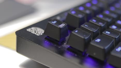 Hand-pressing-a-single-key-on-a-slightly-dusty,-black-keyboard-with-blue-backlit-keys