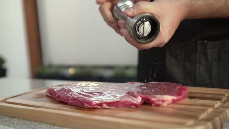 Closeup-of-a-chef-adding-pepper-to-a-raw-beef-steak,-slow-motion