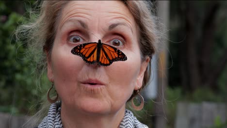 Attractive-middle-aged-woman-looks-surprised-then-goes-cross-eyed-trying-to-look-at-large-Monarch-Butterfly-resting-on-her-nose---close-up---4K,-59