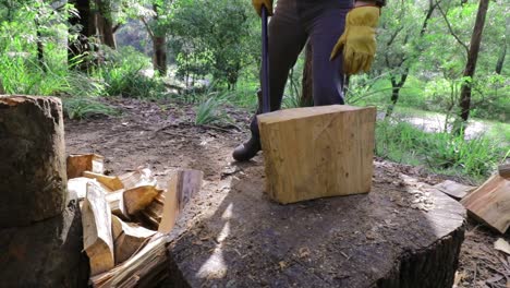 Man-splits-wood-for-winter-fuel-in-Slow-Motion,-Axe-stays-in-chopping-block-as-man-walks-away---green-bushland-nature-setting---close-up-of-log,-man-at-work,-legs,-work-boots-and-work-gloves