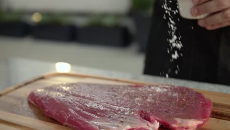 Closeup-of-a-chef-adding-salt-to-a-raw-beef-steak,-slow-motion