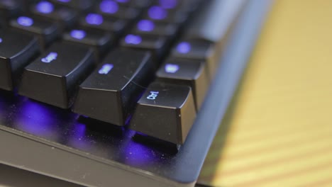 Hand-pressing-a-single-key-on-a-slightly-dusty,-black-keyboard-with-blue-backlit-keys