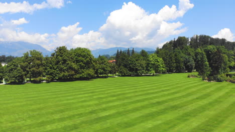 Medium-Wide-angle-Dolly-in-Drone-Shot-of-well-maintained-lawn-and-surrounding-trees-in-Volcji-Potok-Arboretum-during-the-day