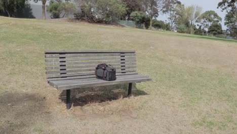 Small-grey-blue-camera-bag-left-in-the-middle-of-a-wooden-park-bench