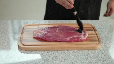 Close-up-of-a-black-silicone-brush-smearing-beef-meat-with-olive-oil-on-a-cutting-board