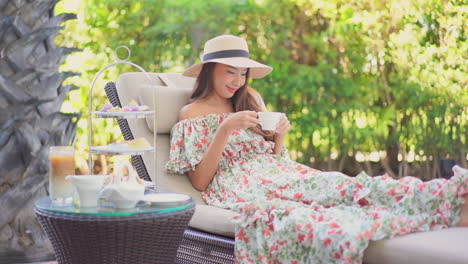 Beautiful-Asian-woman-with-hat-having-afternoon-tea-at-a-luxury-resort