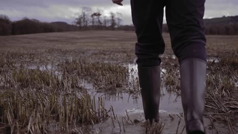 Man-in-wellies-walking-in-farmland-countryside-muddy-puddles,-slow-motion-low-shot
