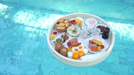 Top-view-on-breakfast-food-tray-floating-on-pool-water