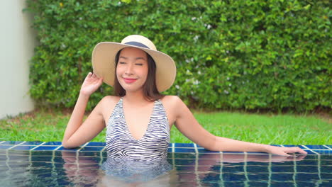 Beautiful-Asian-woman-wearing-hat-relaxes-in-swimming-pool