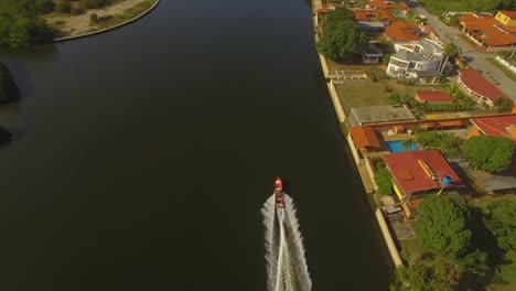 Drone-shot-following-a-small-red-fishing-boat-on-a-dark-water-canal-in-Higuerote,-Venezuela