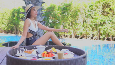 Young-woman-chilling-by-pool-with-tray-of-treat,-coffee,-snack