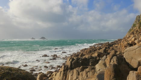 Waves-splashing-on-the-rocky-shoreline-of-Porth-Nanven,-Cornwall,-England,-wide-shot