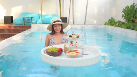 Woman-in-sexy-swimsuit-sharing-floating-tray-with-coffee-and-exotic-treat