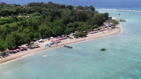 Aerial-view-of-Gili-Trawangan-beach-with-pink-beach-umbrellas-and-tourist-roaming-about