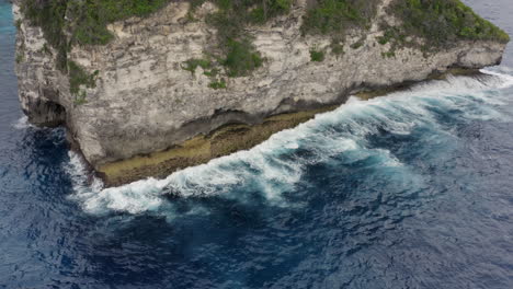Tropical-island-with-huge-steep-cliff-shore-and-ocean-waves-crushing-ashore,-Nusa-Penida,-Bali,-Indonesia