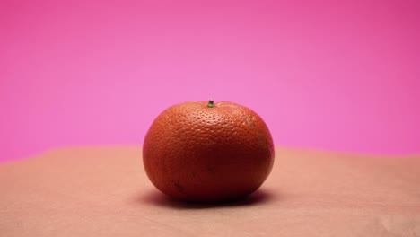 Ripe-mandarine,-rotate-on-pink-and-old-paper-background-4k-video-colorized