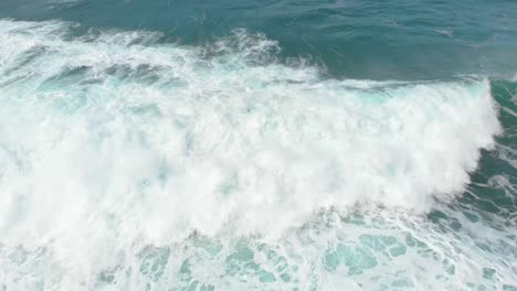 An-interesting-aerial-birds-eye-view-shot-following-a-wave-crashing-into-shore-as-the-white-wash-swirls-around-the-water