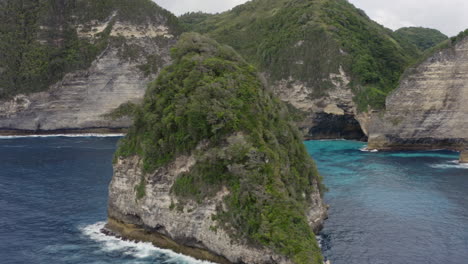Fly-by-along-the-steep-coast-line-of-Nusa-Penida-with-remote-islands-and-ocean-waves-crushing-ashore,-Bali,-Indonesia