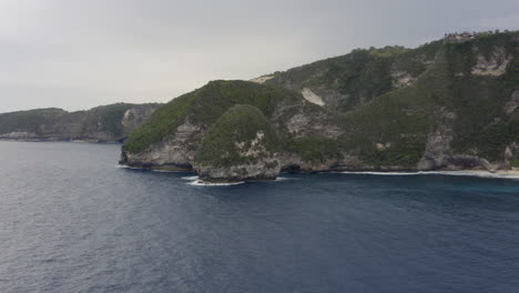 Fliegen-Sie-Entlang-Der-Steilen-Küstenlinie-Von-Nusa-Penida-Mit-Abgelegenen-Inseln-Und-Meereswellen,-Die-An-Land-Brechen,-Bali,-Indonesien
