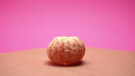 Reife-Geschälte-Mandarine,-Rotieren-Auf-Rosafarbenem-Und-Altem-Papierhintergrund-4k-Video-Mit-Farbkorrektur