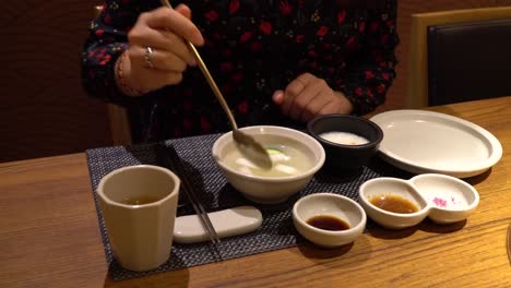 Mujer-Comiendo-Kimchi-De-Agua-De-Rábano-Coreano-Dongchimi,-Mostrando-En-Primer-Plano-De-La-Cuchara-En-El-Restaurante