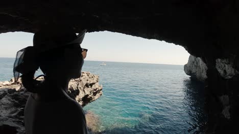 A-young-girl-looking-at-the-sea-from-inside-a-sea-cave-near-Paphos,-Cypris