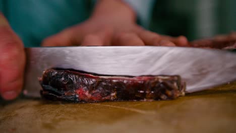 Close-up-view-of-chef-hand-slicing-the-steak-with-Steel-knife-on-a-wooden-chop-board