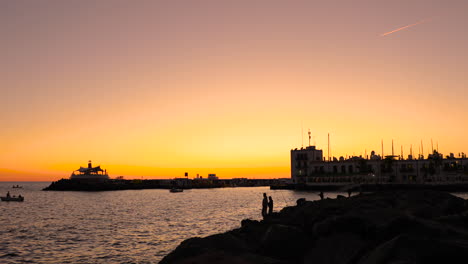 Fischer-Am-Pier-Und-An-Der-Küste-Während-Des-Orangefarbenen-Sonnenuntergangs,-Der-Angelschnur-Auf-Dem-Offenen-Meer-Wirft