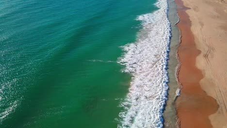Aerial-shot-of-long-waves-breaking-into-a-empty-sandy-beach